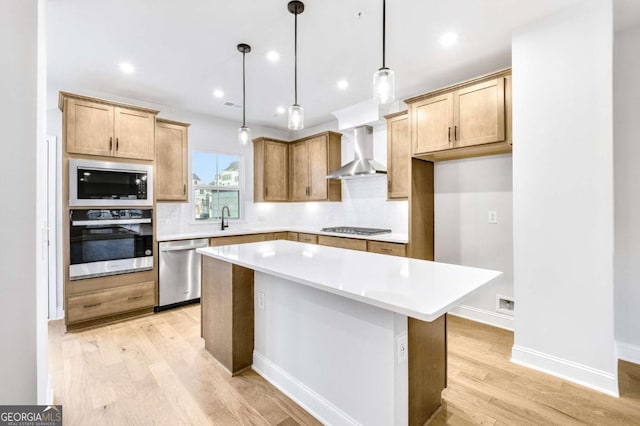 kitchen featuring stainless steel appliances, sink, wall chimney range hood, decorative light fixtures, and a center island