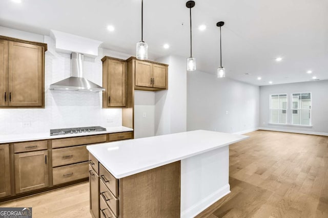 kitchen featuring light wood-type flooring, decorative light fixtures, stainless steel gas cooktop, and wall chimney range hood