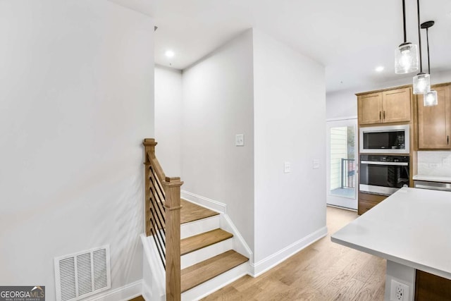 kitchen with oven, built in microwave, decorative light fixtures, and light hardwood / wood-style flooring