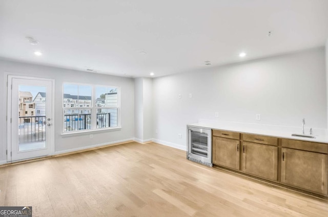 bar with sink, beverage cooler, and light wood-type flooring