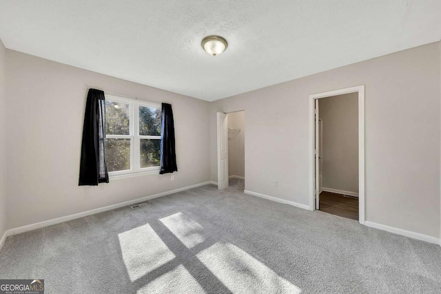 unfurnished bedroom with a textured ceiling, a walk in closet, light colored carpet, and a closet