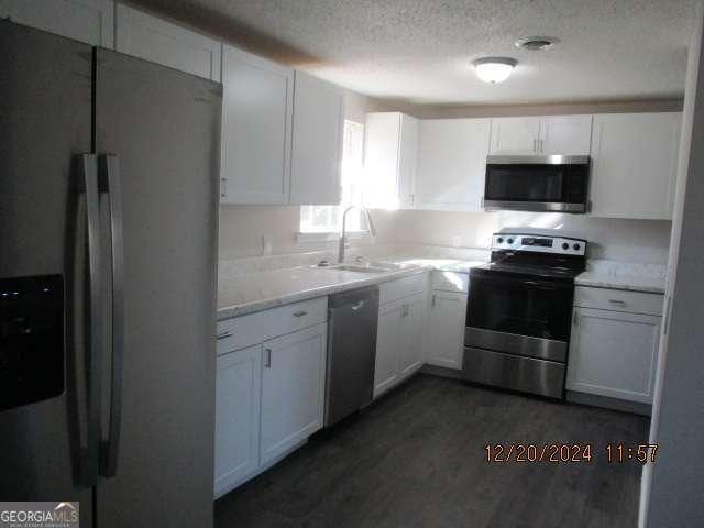 kitchen with light stone countertops, appliances with stainless steel finishes, sink, white cabinets, and dark hardwood / wood-style floors