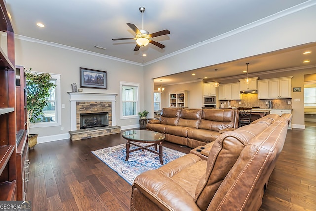 living room with ceiling fan with notable chandelier, a stone fireplace, ornamental molding, and a wealth of natural light