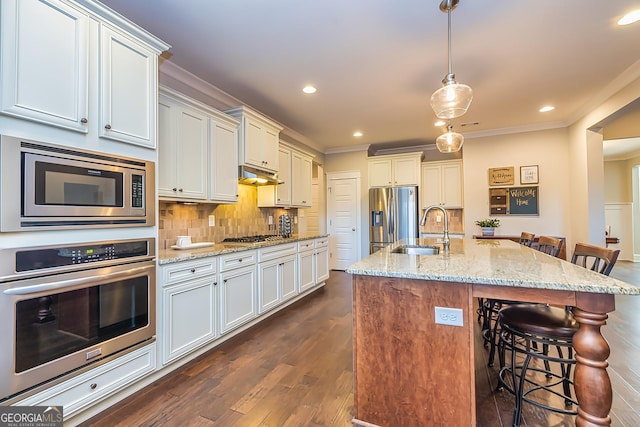 kitchen with sink, an island with sink, a kitchen bar, white cabinetry, and stainless steel appliances