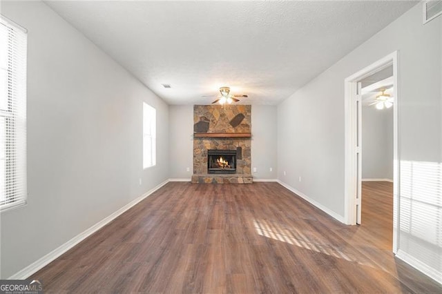 unfurnished living room with a stone fireplace, dark hardwood / wood-style flooring, and a textured ceiling