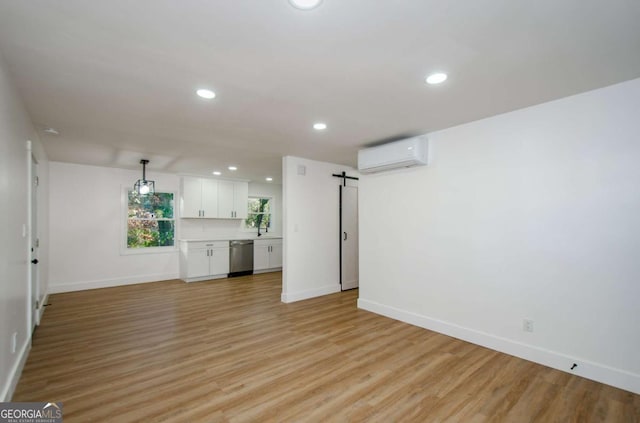 unfurnished living room with a barn door, sink, a wall mounted air conditioner, and light wood-type flooring