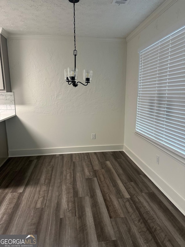 unfurnished dining area with dark hardwood / wood-style flooring, a chandelier, a textured ceiling, and ornamental molding