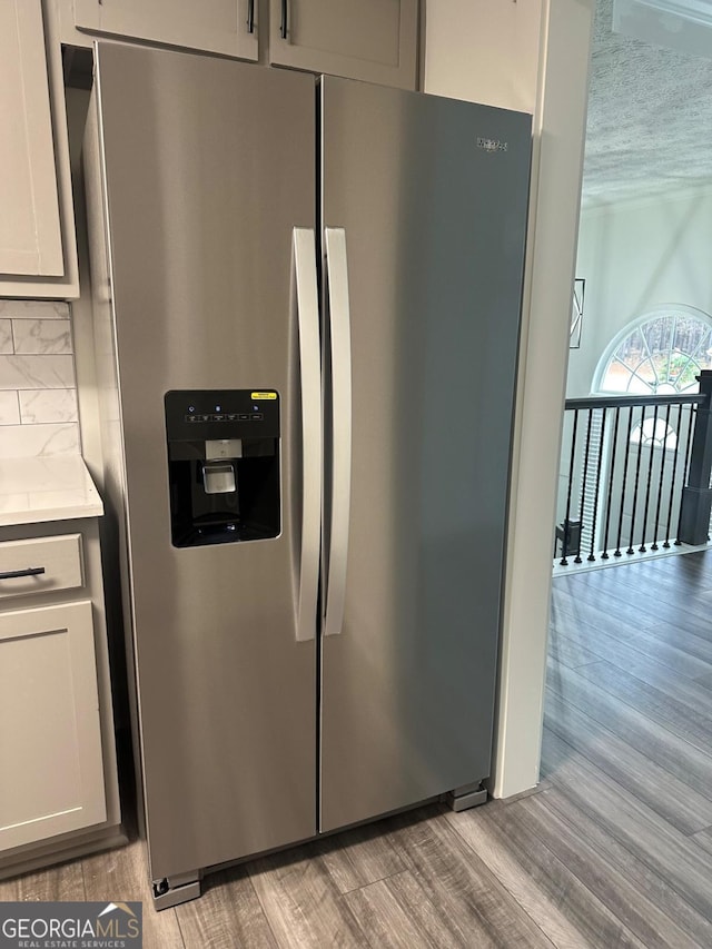 interior details featuring decorative backsplash, stainless steel refrigerator with ice dispenser, light wood-type flooring, and white cabinetry