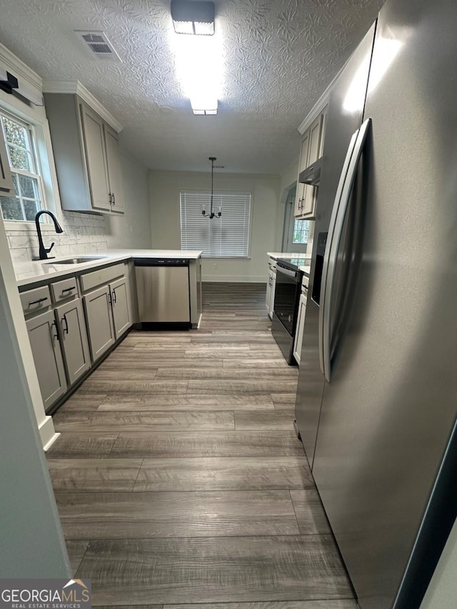 kitchen featuring gray cabinetry, sink, hanging light fixtures, backsplash, and appliances with stainless steel finishes