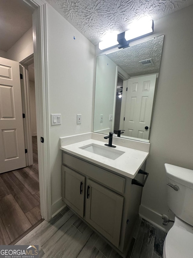 bathroom featuring hardwood / wood-style floors, vanity, a textured ceiling, and toilet