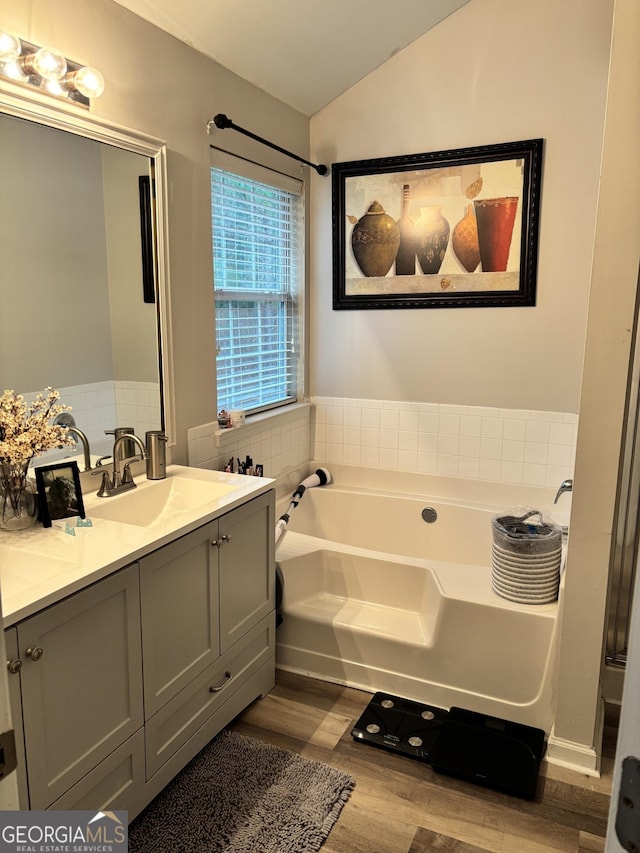 bathroom with hardwood / wood-style floors, vanity, a tub to relax in, and vaulted ceiling