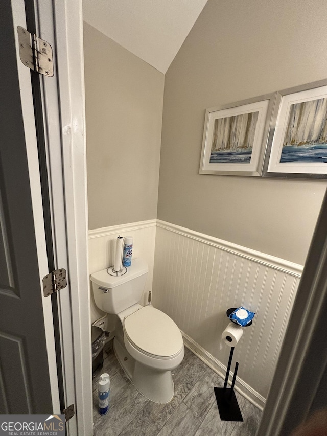 bathroom featuring lofted ceiling, toilet, wood finished floors, and wainscoting