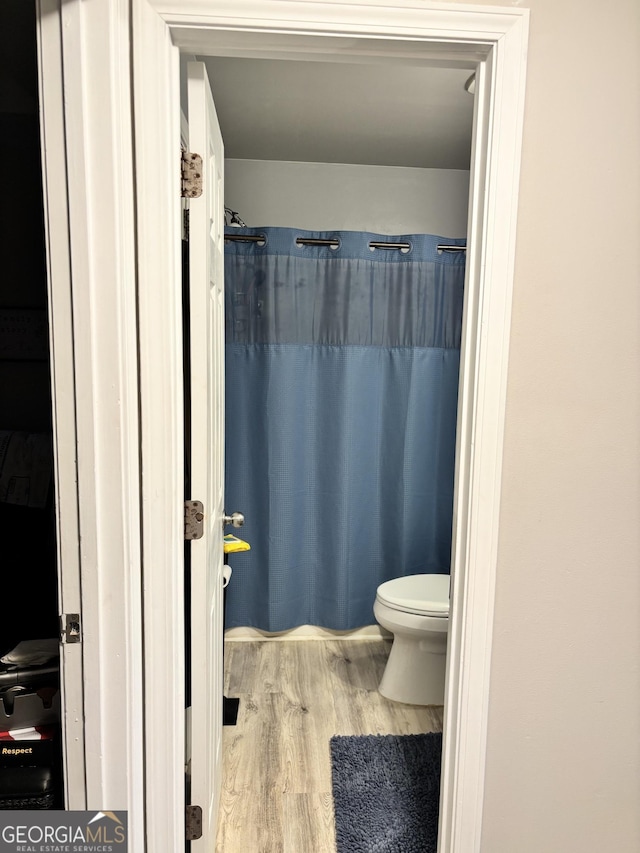 bathroom with hardwood / wood-style floors, a shower with shower curtain, and toilet