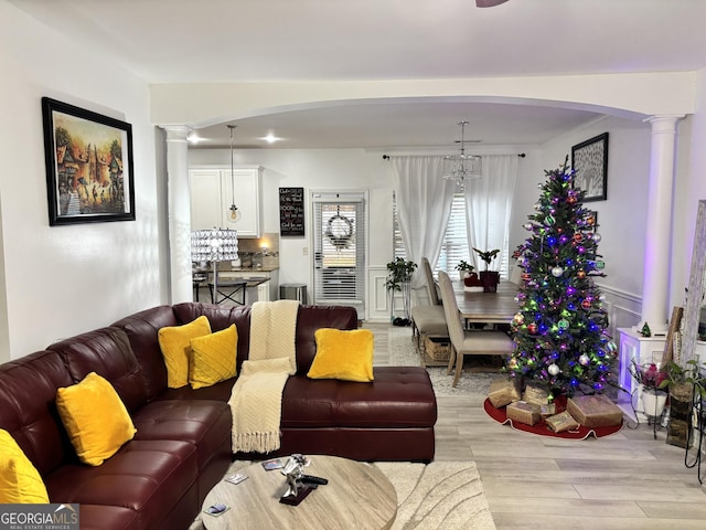 living room featuring light wood-type flooring, decorative columns, and a notable chandelier