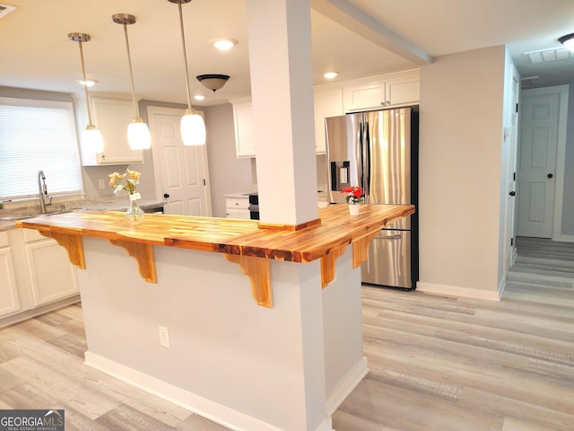 kitchen featuring stainless steel fridge, decorative light fixtures, white cabinets, butcher block countertops, and a breakfast bar area