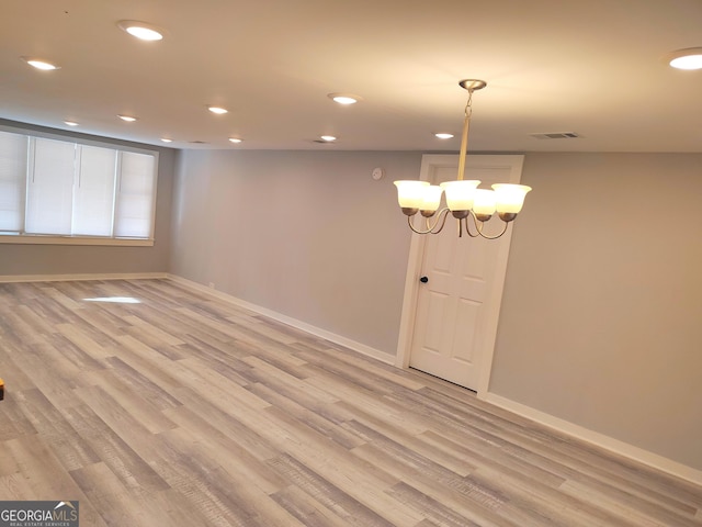 spare room with light wood-type flooring and a chandelier