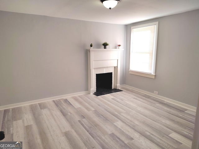 unfurnished living room featuring light wood-type flooring and a brick fireplace