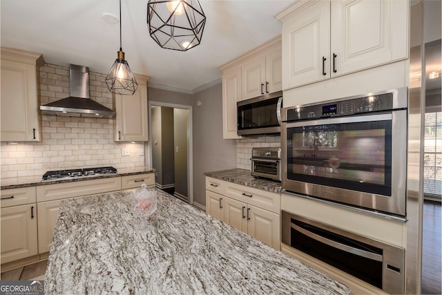 kitchen featuring appliances with stainless steel finishes, light stone counters, decorative backsplash, decorative light fixtures, and wall chimney exhaust hood