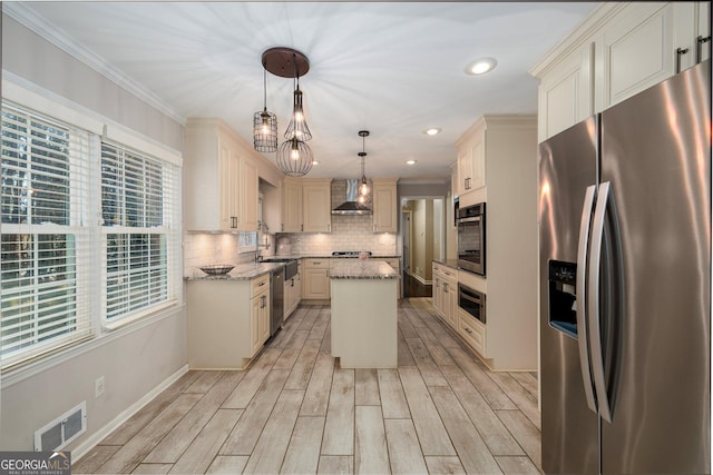 kitchen with wall chimney exhaust hood, light stone counters, decorative light fixtures, a center island, and appliances with stainless steel finishes