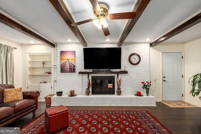 living room featuring ceiling fan, a fireplace, dark hardwood / wood-style flooring, built in shelves, and beamed ceiling