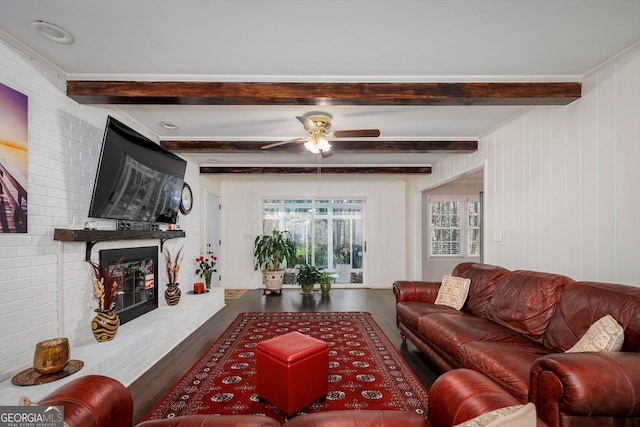 living room featuring beamed ceiling, a brick fireplace, hardwood / wood-style flooring, and ceiling fan