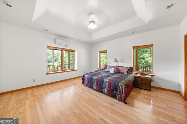 bedroom with a wall mounted air conditioner, a raised ceiling, and light hardwood / wood-style flooring