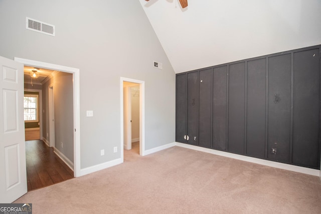 unfurnished bedroom featuring light colored carpet, ornamental molding, high vaulted ceiling, and ceiling fan