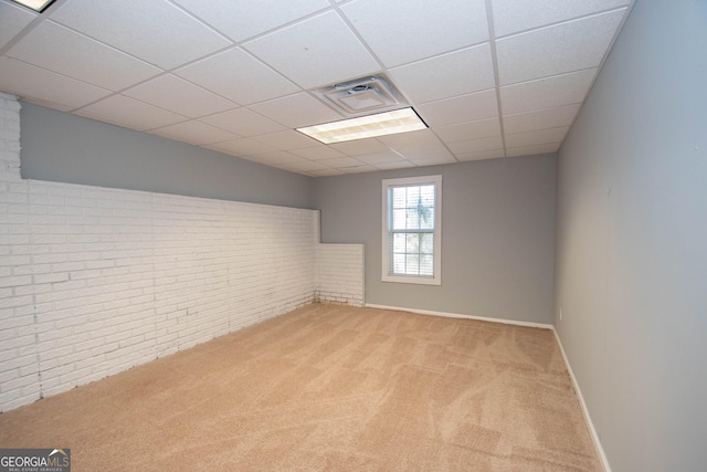 basement with a drop ceiling, light colored carpet, and brick wall