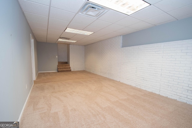 basement featuring brick wall, light carpet, and a drop ceiling