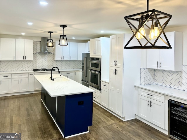 kitchen with white cabinetry, beverage cooler, wall chimney range hood, light stone counters, and a kitchen island with sink