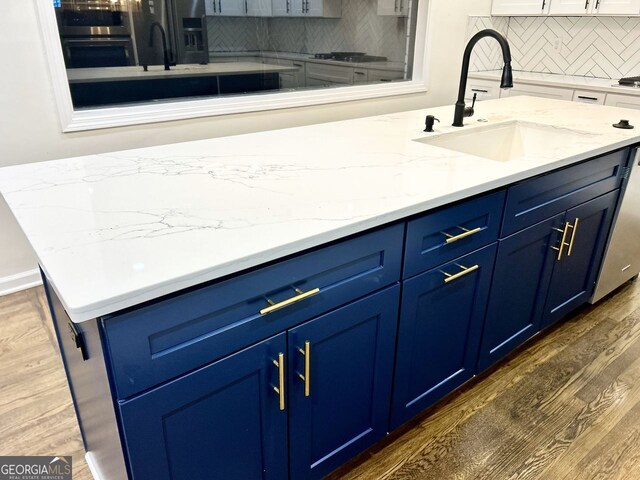 kitchen with dark wood-type flooring, sink, decorative backsplash, blue cabinetry, and stainless steel appliances