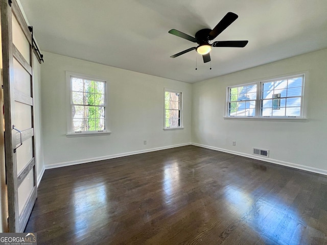 unfurnished room with ceiling fan, a barn door, and dark wood-type flooring