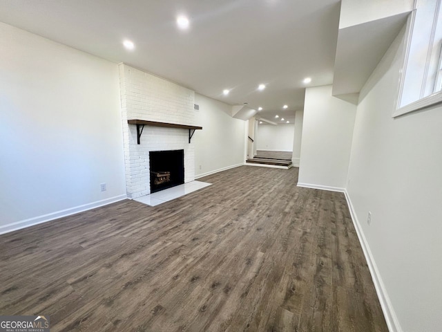 unfurnished living room featuring dark wood-type flooring and a brick fireplace