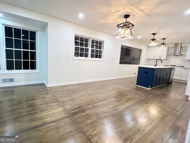 kitchen with pendant lighting, a kitchen island with sink, wall chimney range hood, decorative backsplash, and white cabinetry