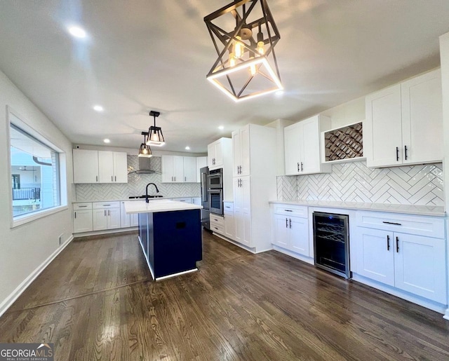 kitchen featuring a kitchen island with sink, hanging light fixtures, wine cooler, dark hardwood / wood-style floors, and white cabinetry