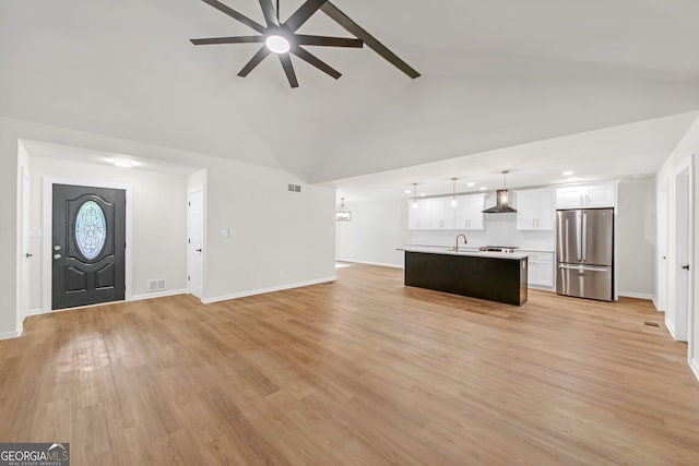 unfurnished living room with ceiling fan, sink, light hardwood / wood-style flooring, and vaulted ceiling