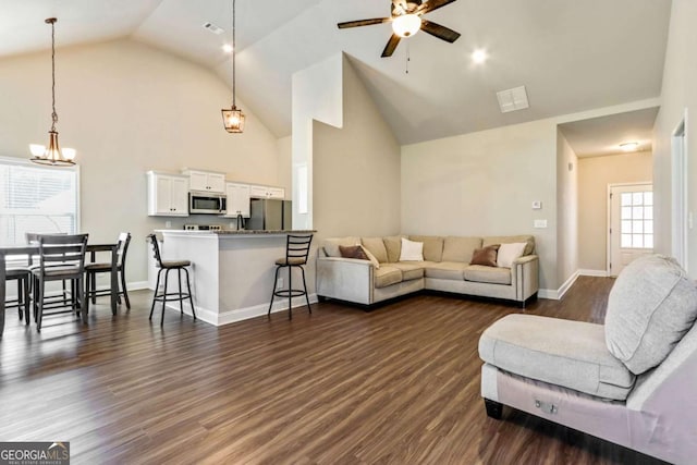 living room with ceiling fan with notable chandelier, dark hardwood / wood-style flooring, and high vaulted ceiling