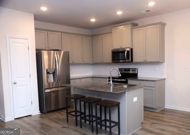 kitchen featuring dark stone counters, a breakfast bar area, gray cabinets, a kitchen island with sink, and appliances with stainless steel finishes