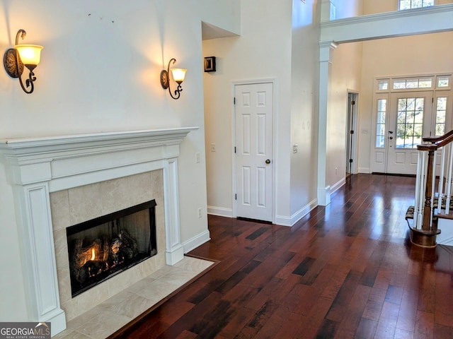 living room featuring a high ceiling, dark wood-type flooring, and a tiled fireplace