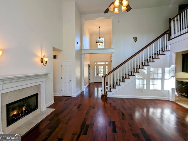 foyer featuring a tile fireplace, ceiling fan, a towering ceiling, and dark wood-type flooring