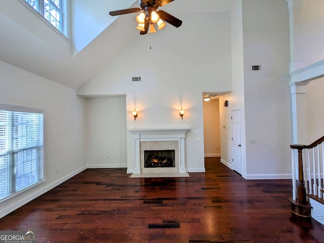 unfurnished living room featuring ceiling fan, a fireplace, a towering ceiling, and dark hardwood / wood-style floors