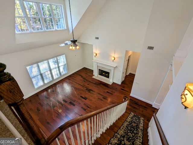 living room featuring a high end fireplace, high vaulted ceiling, ceiling fan, and dark wood-type flooring