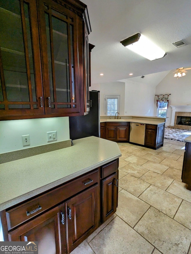 kitchen featuring a tile fireplace, ceiling fan, sink, stainless steel dishwasher, and lofted ceiling