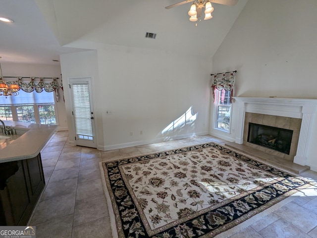 living room featuring a fireplace, high vaulted ceiling, ceiling fan with notable chandelier, and light tile patterned floors