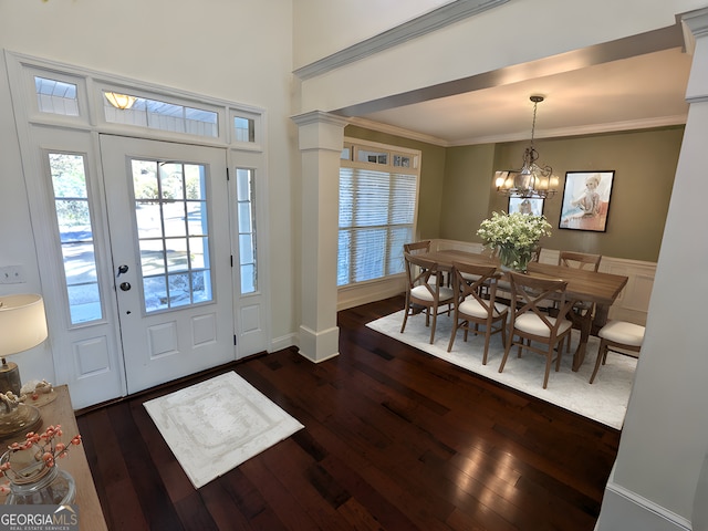 entrance foyer with decorative columns, dark hardwood / wood-style flooring, a chandelier, and ornamental molding