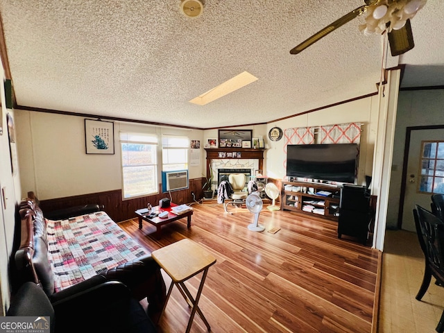 living room featuring ceiling fan, wood walls, a textured ceiling, and a skylight