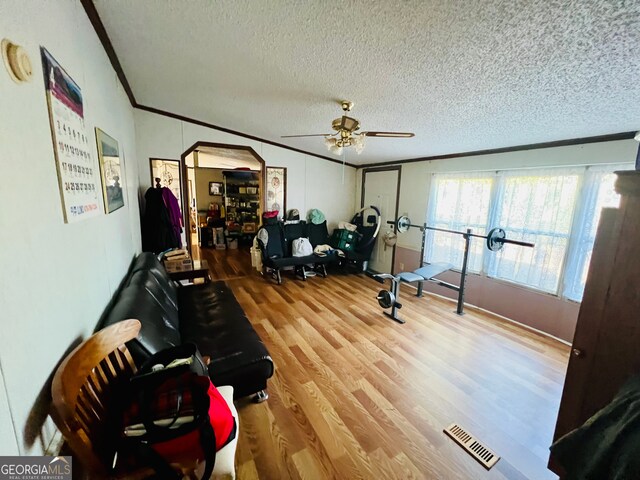 workout room featuring wood-type flooring, a textured ceiling, ceiling fan, and ornamental molding