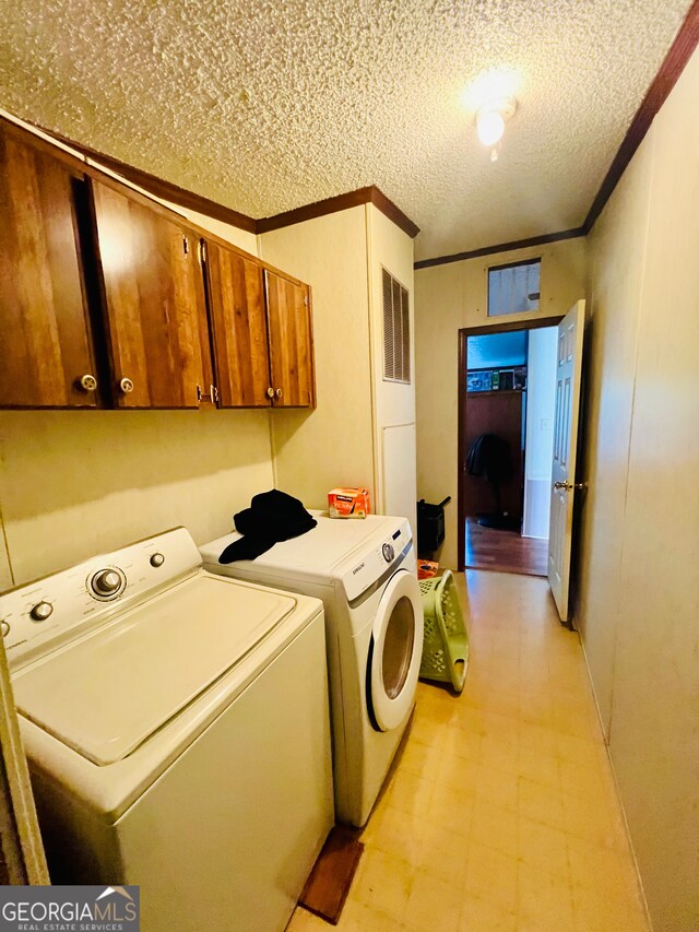 washroom featuring cabinets, a textured ceiling, washing machine and dryer, and ornamental molding