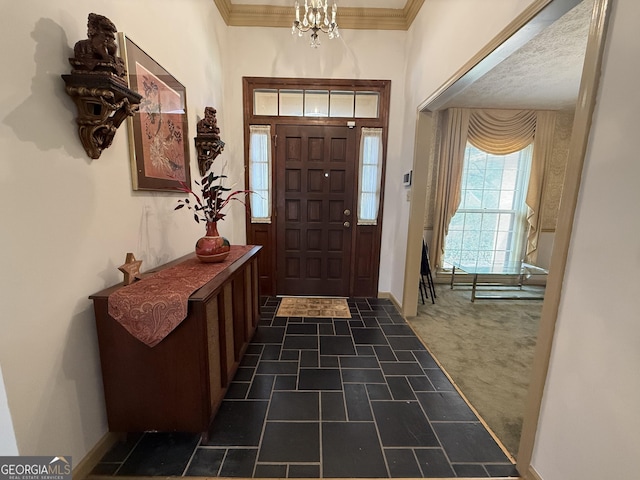 foyer entrance with a chandelier, a textured ceiling, dark colored carpet, and ornamental molding