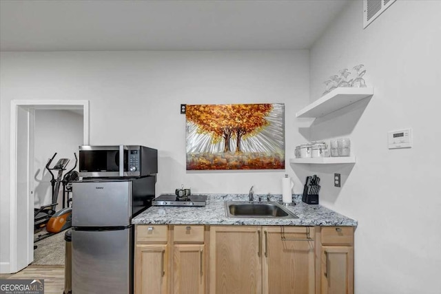 kitchen featuring sink, stainless steel appliances, light stone counters, light brown cabinetry, and light wood-type flooring